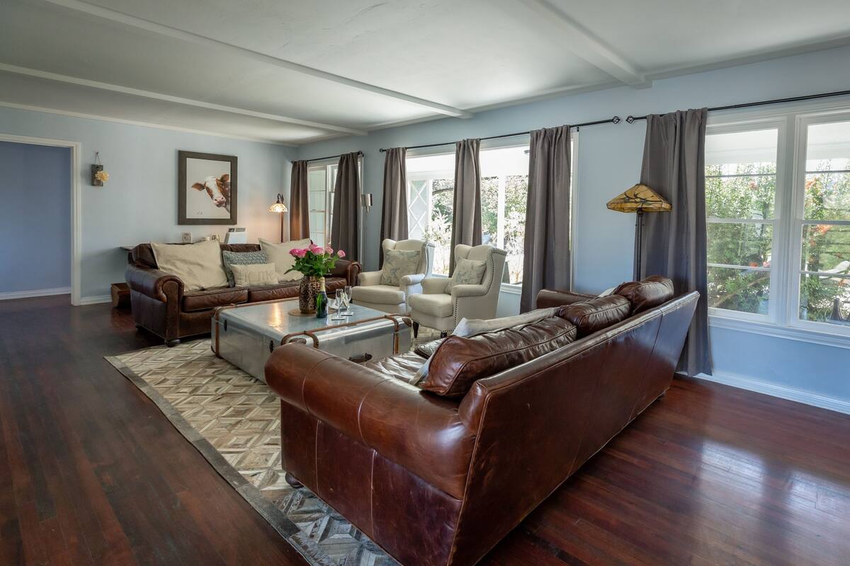 A spacious living room with a brown leather sofa, a beige armchair, and a glass coffee table.