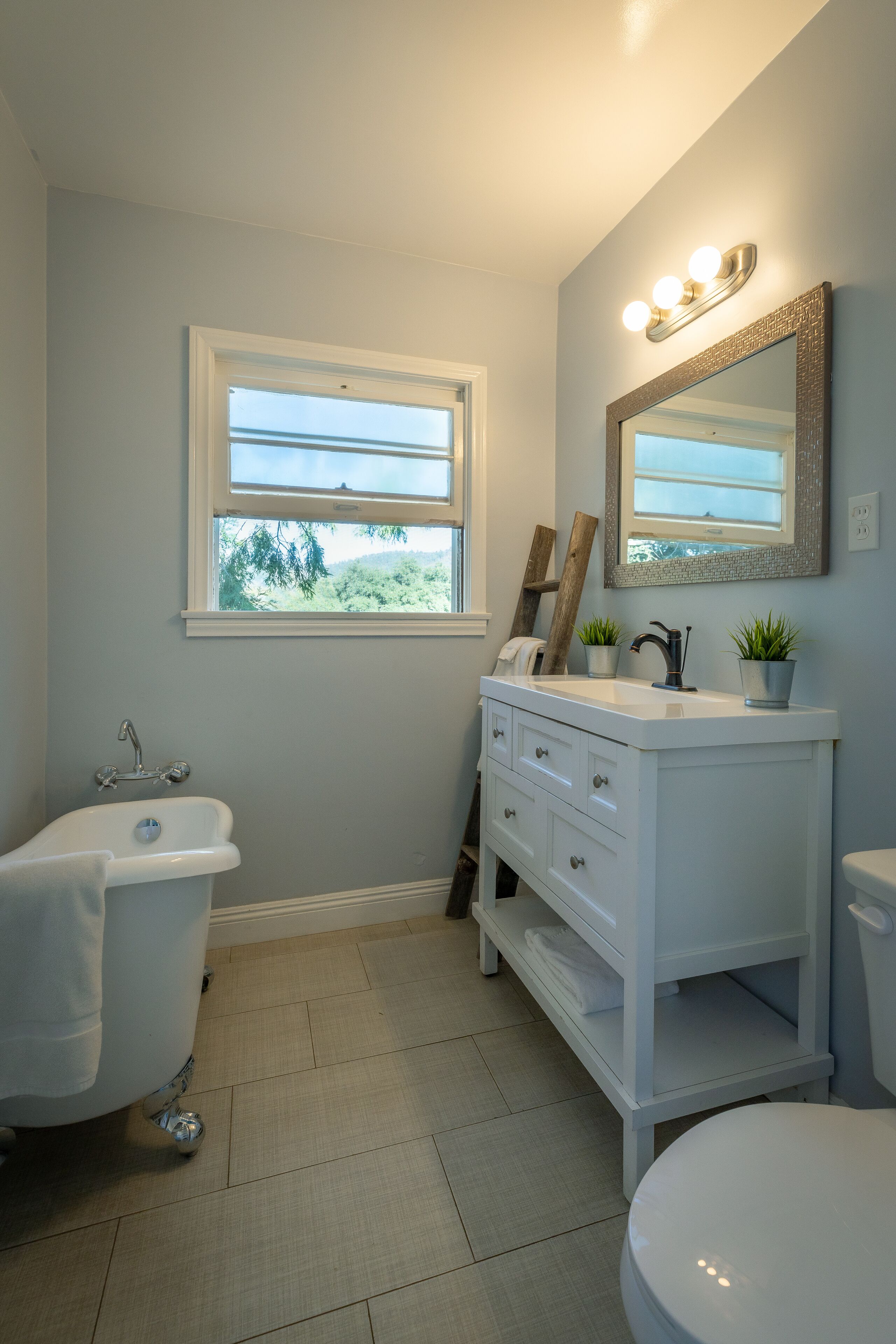 A bathroom with a white bathtub, a sink with a mirror above it, and a window providing natural light.