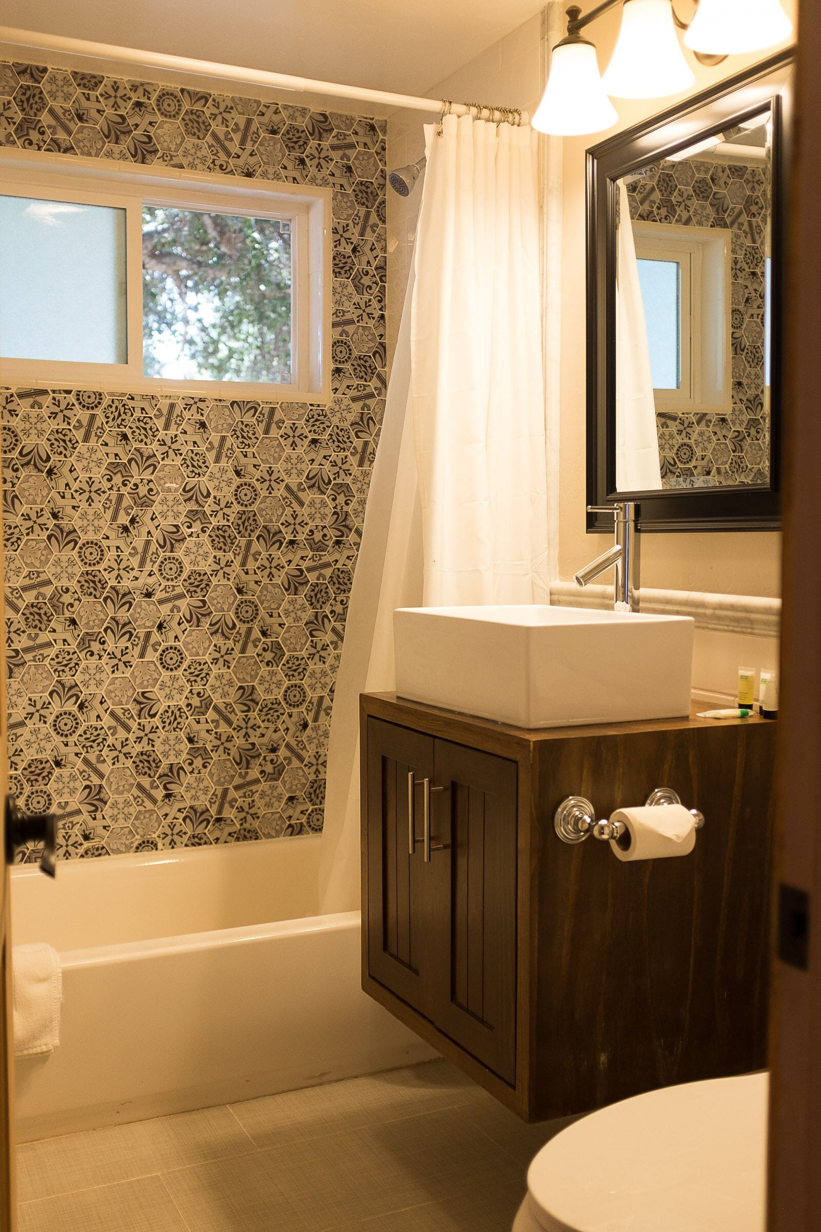 Un baño con pared estampada, ventana, bañera, lavabo y espejo.