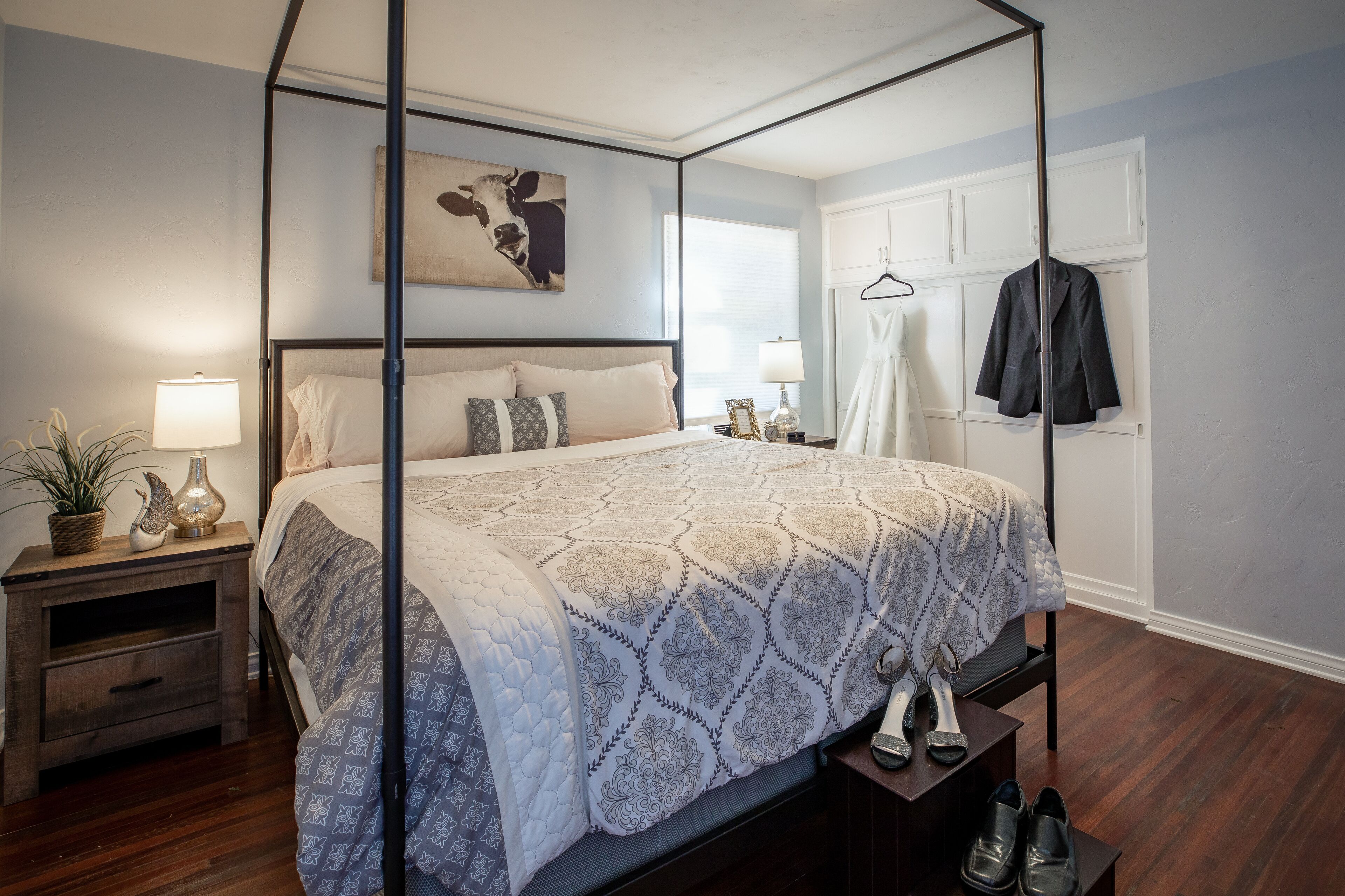 Un lit à baldaquin avec une couvre-lit à motifs, une table de chevet avec une lampe, un porte-manteau mural et un tableau encadré accroché au mur.