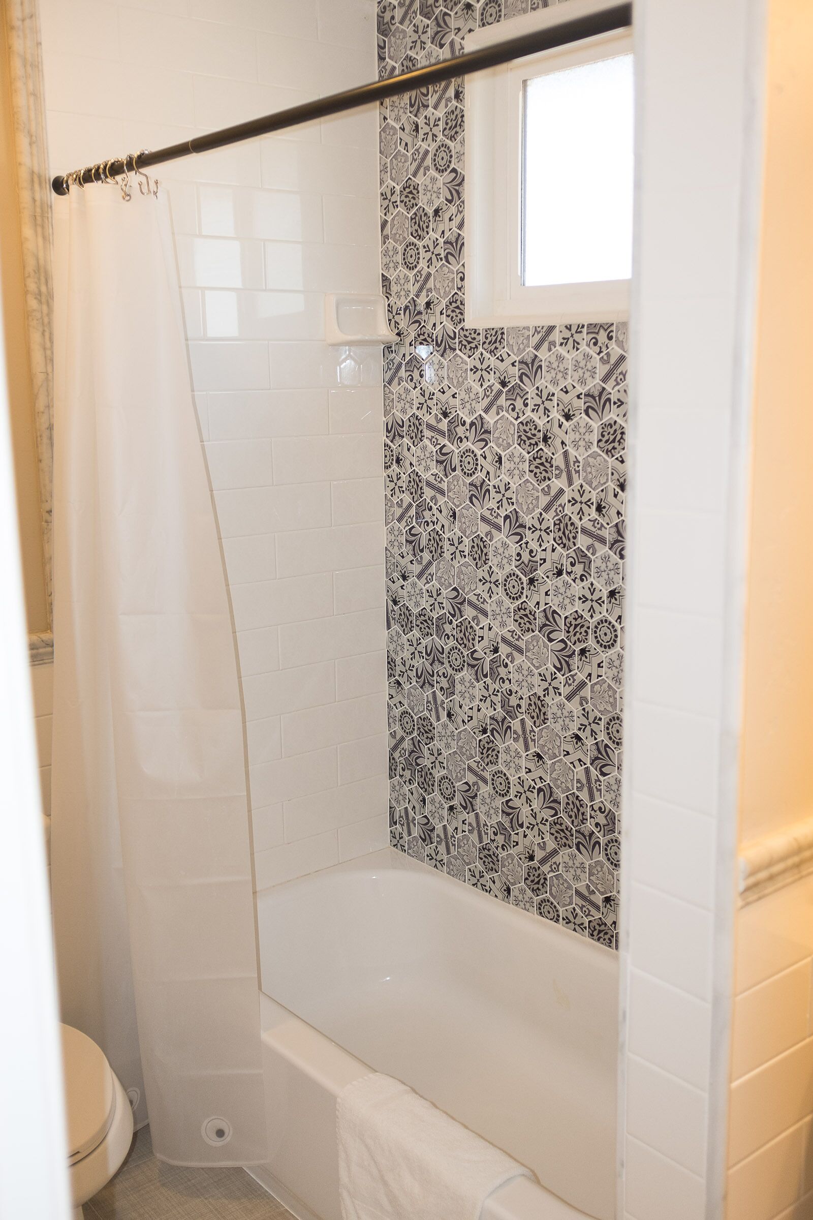A shower with a glass door, a white bathtub, and a patterned tile wall.