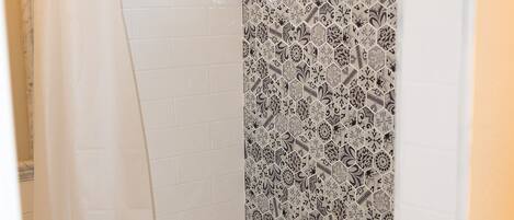 A shower with a glass door, a white bathtub, and a patterned tile wall.