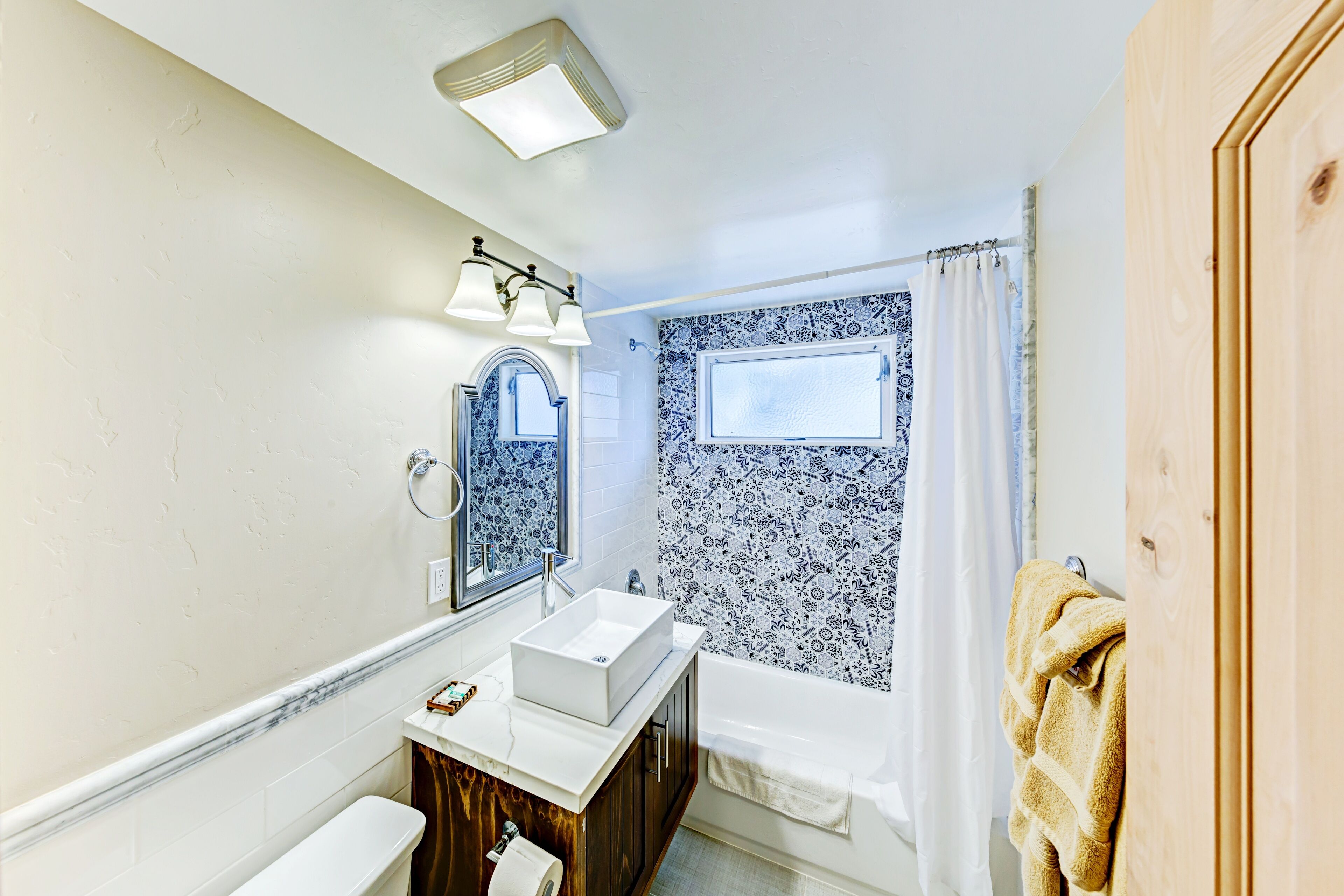 Un bagno con lavandino, mobile lavabo e vasca da bagno bianchi. Si vede una finestra con tenda e un asciugamano appeso al muro.