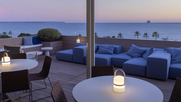 Terraza en la azotea con vista al mar, con un conjunto de sofás y mesas redondas con faroles.