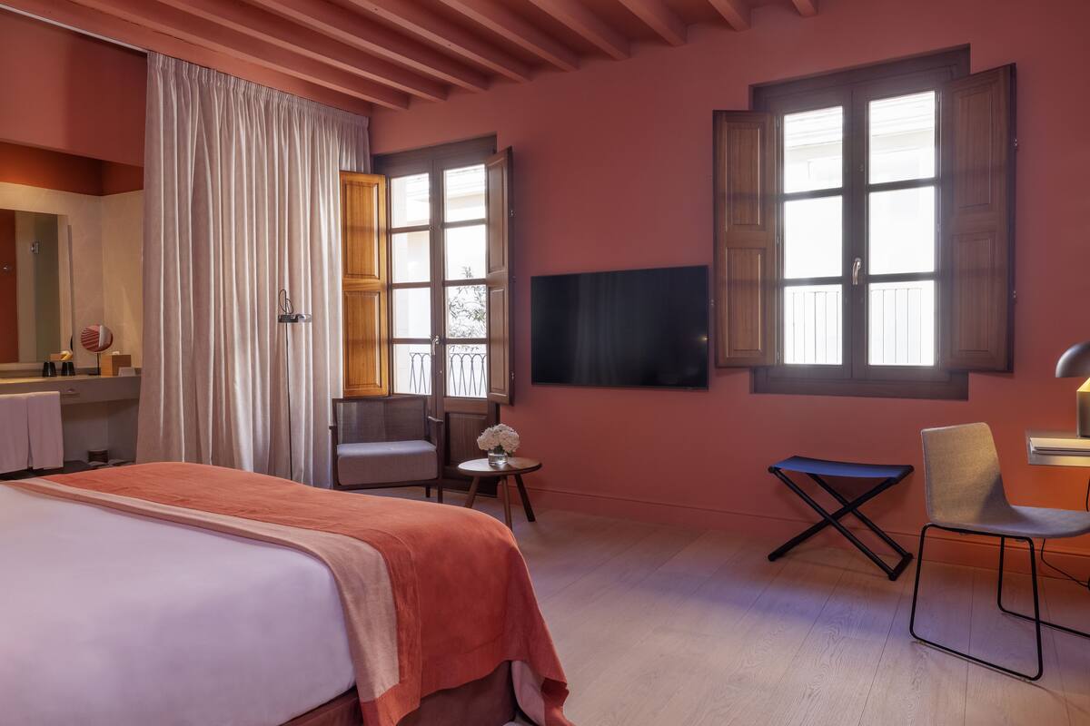 A hotel room with a bed, a desk, a chair, a TV, and a window with curtains.