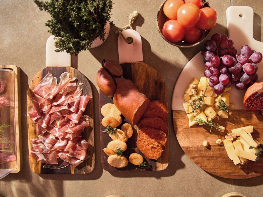 Diversos alimentos como carnes, quesos y frutas dispuestos sobre tablas de madera.