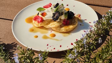 A dessert on a white plate with fruit and sauce, surrounded by greenery.