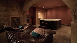 Un cuarto de spa con pared de piedra, un jacuzzi y dos sillas de mimbre con toallas.