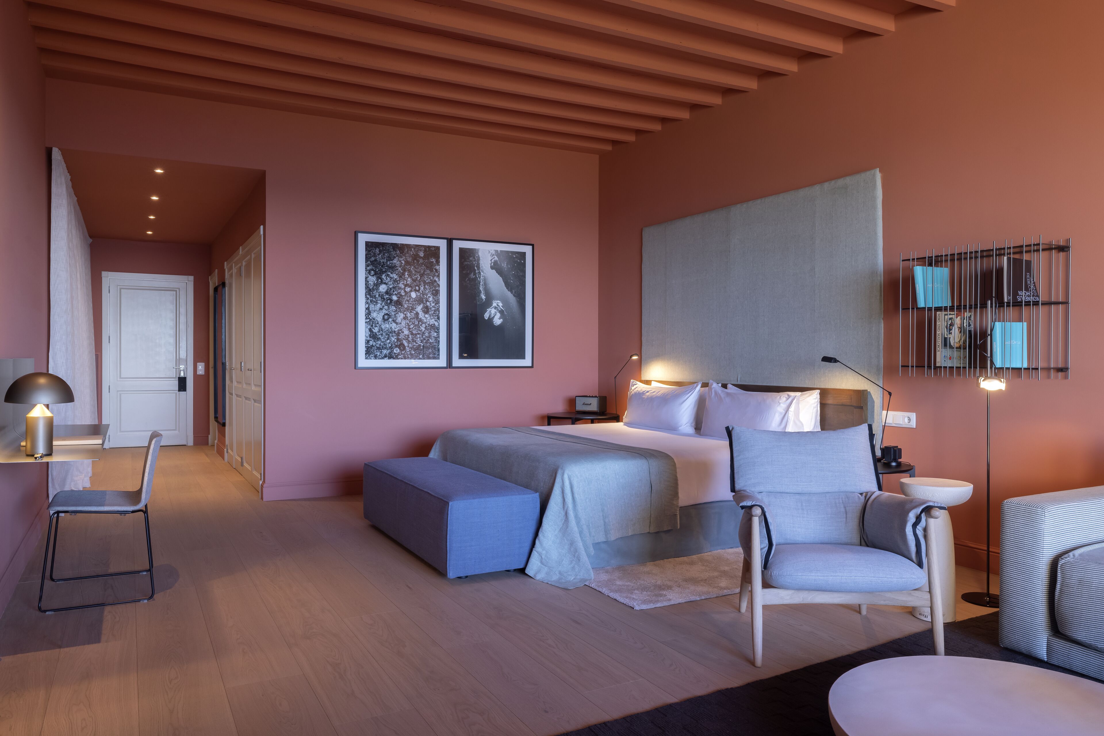 A modern bedroom with a bed, bedside tables, a chair, a bench, and artwork on the wall.