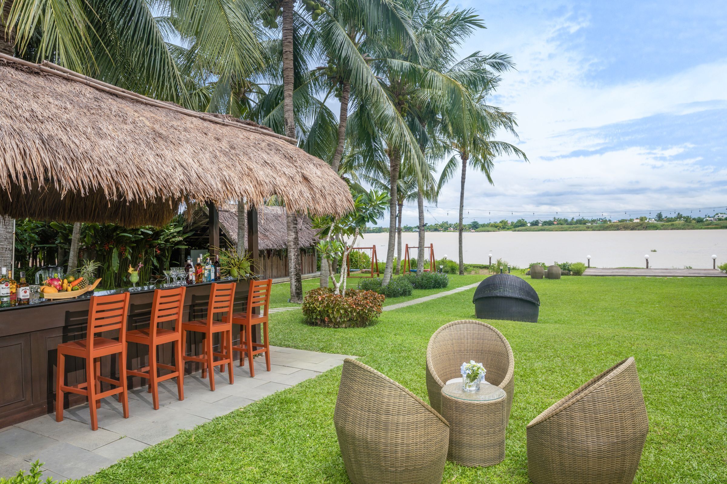 A thatched-roof bar area with wooden chairs, wicker furniture, and a view of the beach.