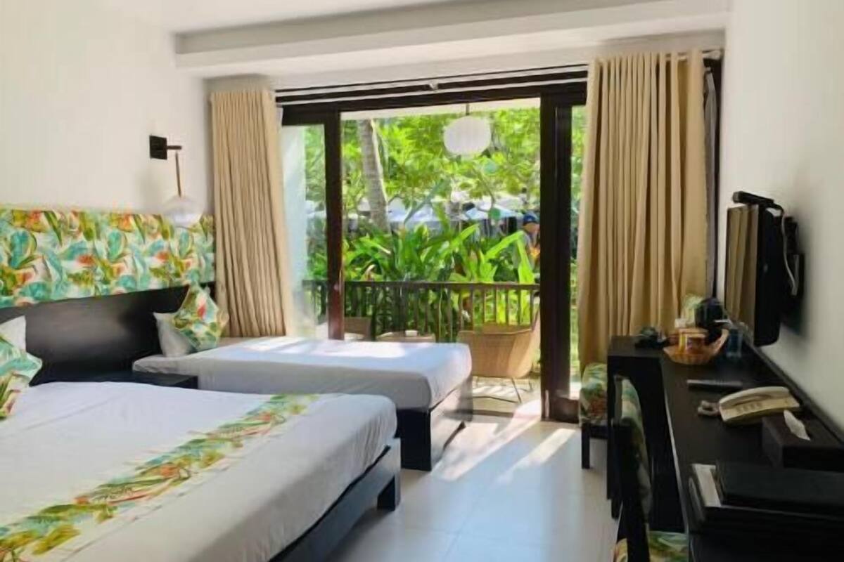 Une chambre d’hôtel équipée d’un lit, d’un bureau, d’une chaise, d’une télévision et d’un balcon agrémenté de plantes.