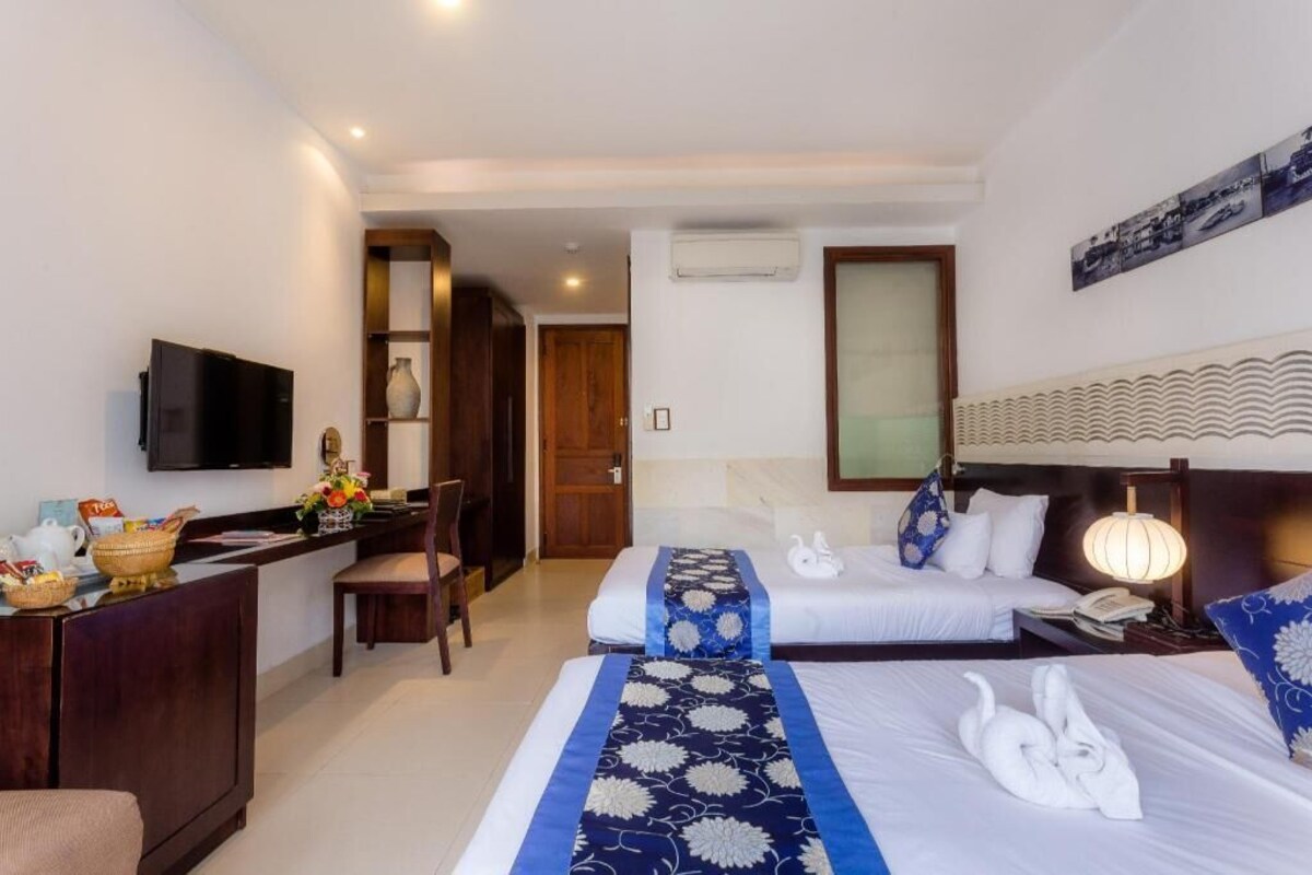 A hotel room with a desk, two beds, a TV, and a mirror.