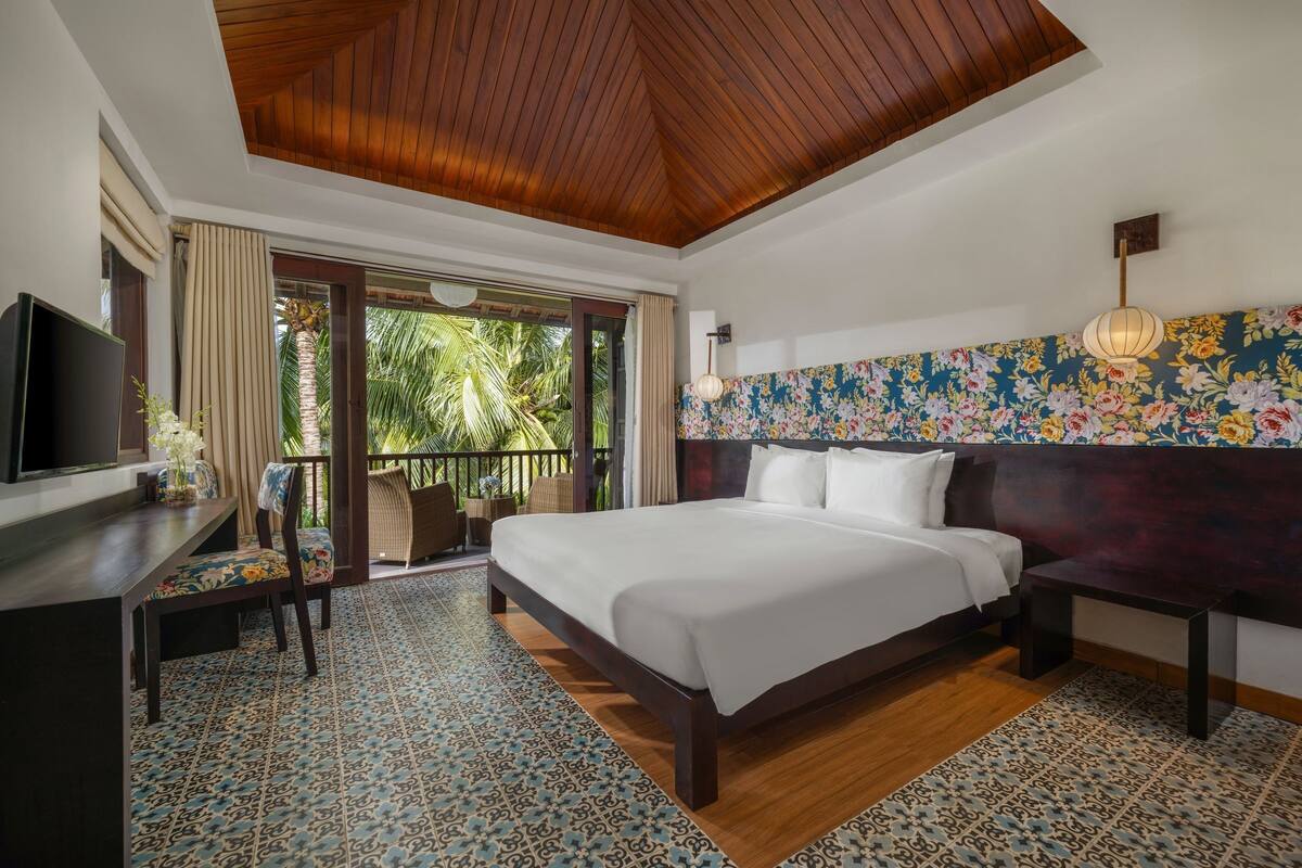 A spacious bedroom with a large bed, a desk, and a television.
