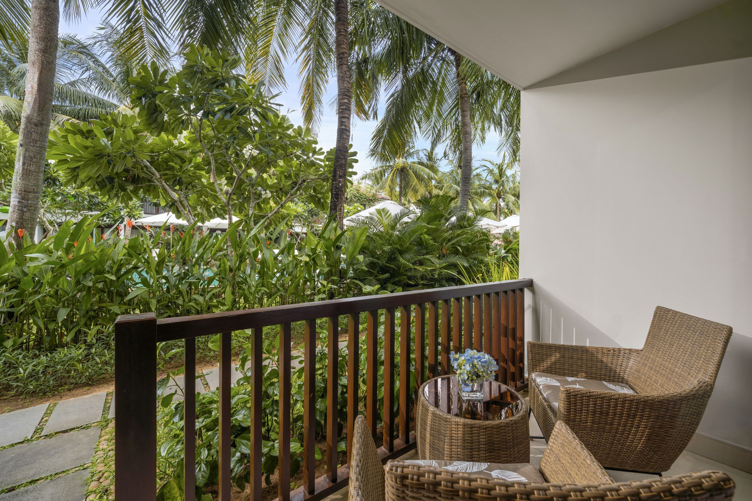 A balcony with wicker furniture, a vase with flowers, and lush tropical plants.