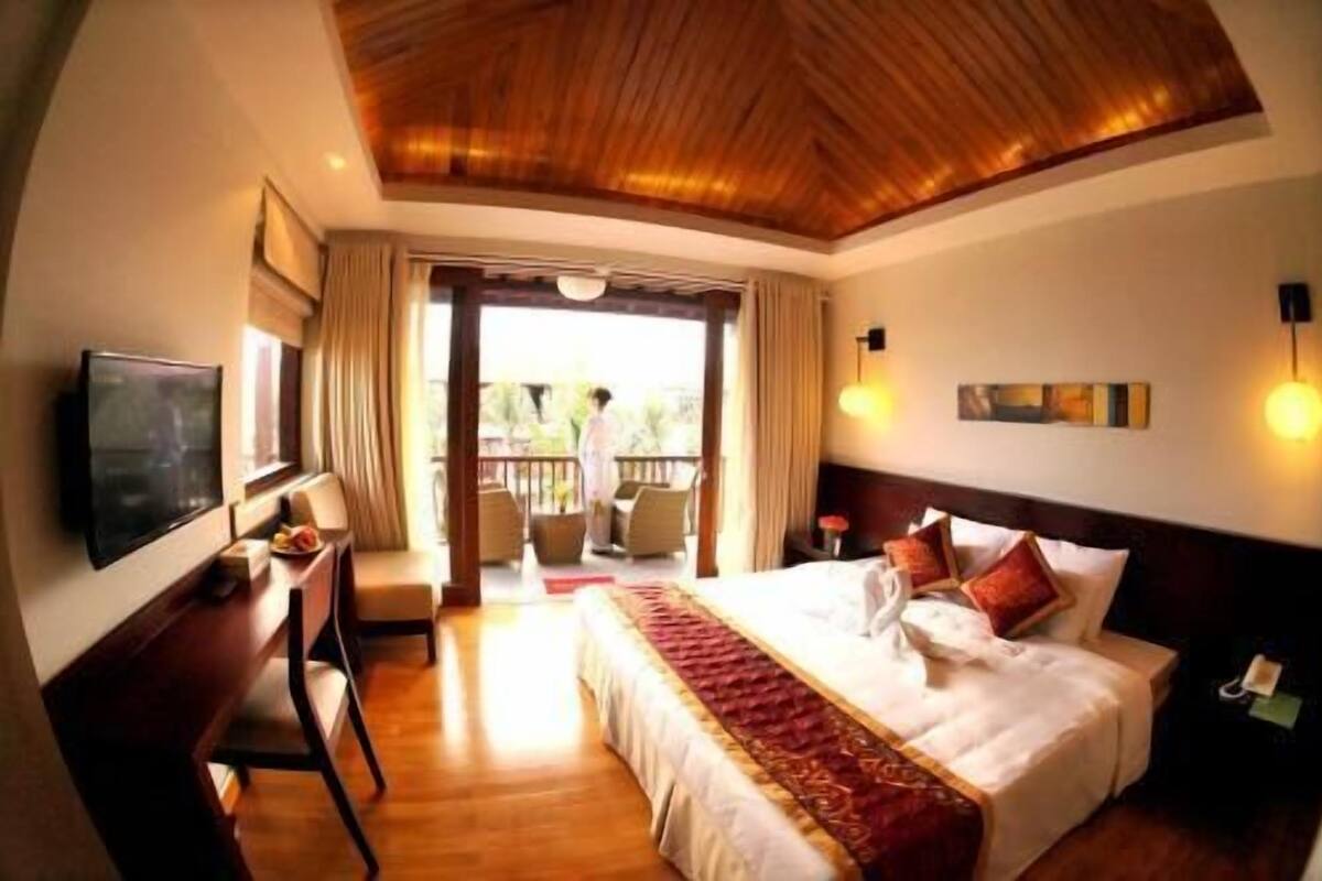 Une chambre d’hôtel avec un plafond en bois, un lit avec une literie rouge et blanche, une télévision, un bureau et un balcon avec des sièges d’extérieur.