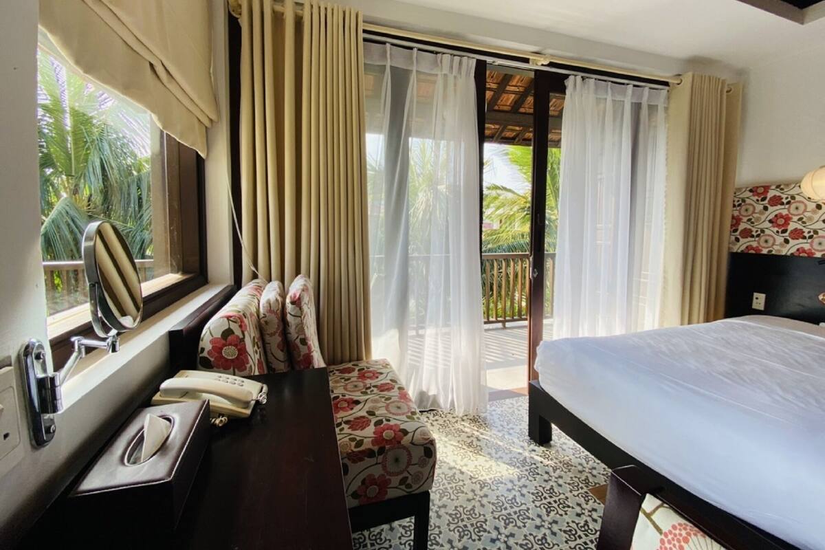 Une chambre d’hôtel avec un lit, un bureau avec un téléphone, une chaise et une fenêtre avec des rideaux.