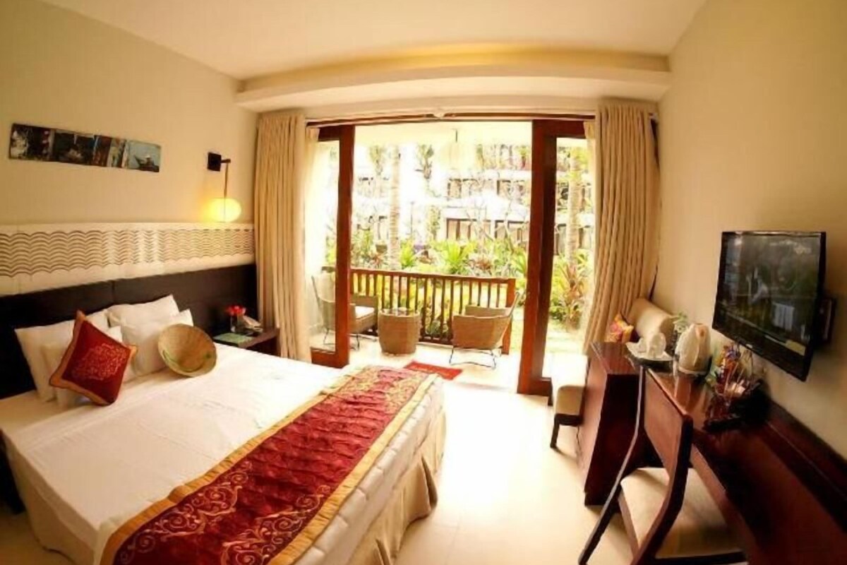 A hotel room with a bed, a desk, a television, and a balcony with outdoor furniture.