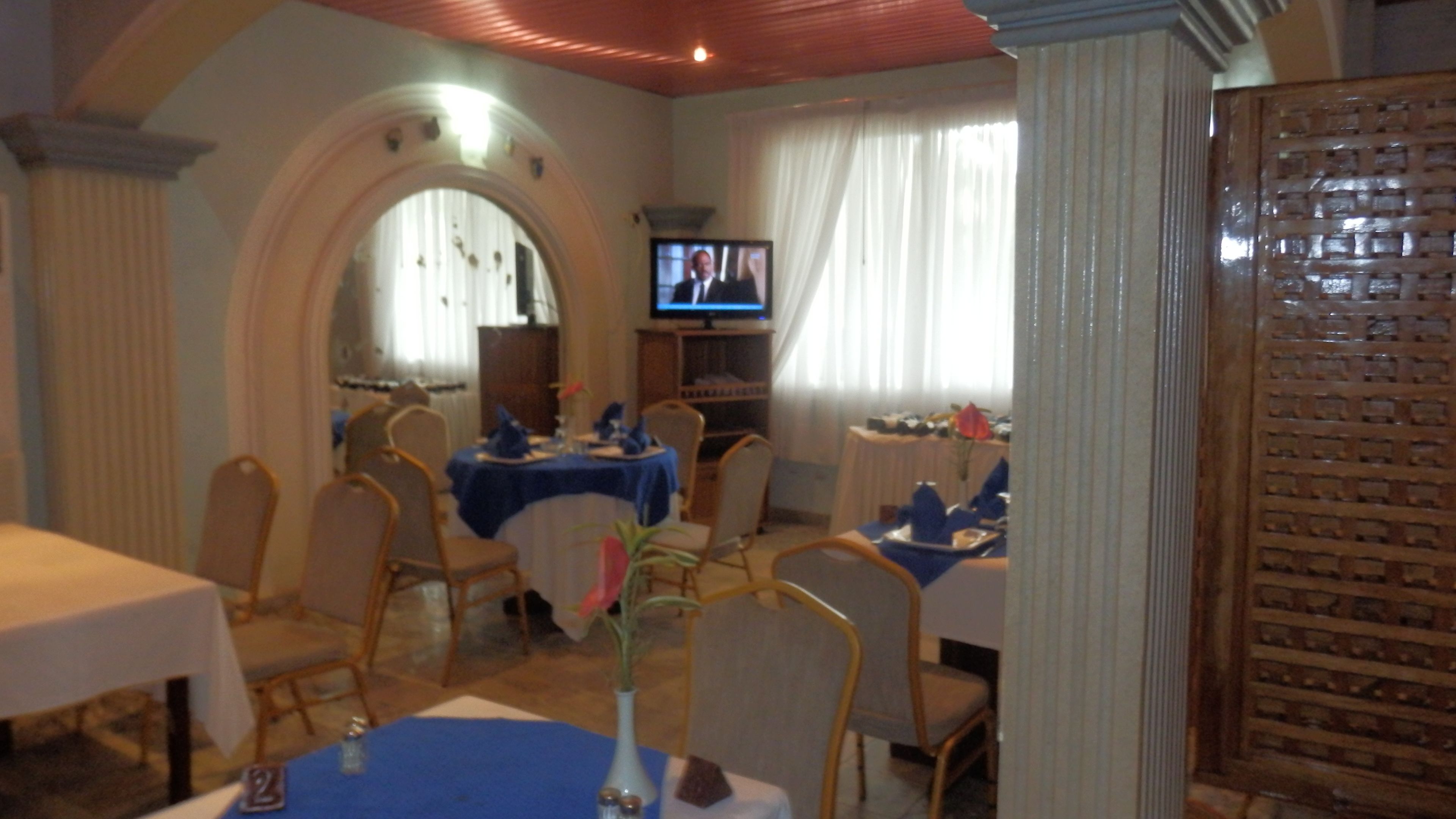 A dining area with tables set for a meal, a television in the background, and a decorative wooden panel on the right.