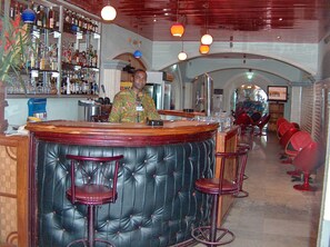 Eine Bar mit einer Theke, ledernen Barhocker und einer Auswahl an Flaschen in Regalen.