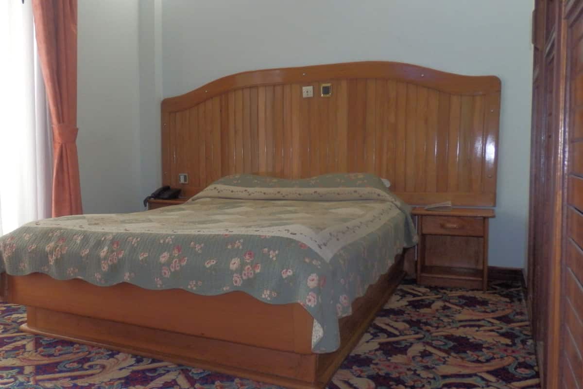 A single bed with a floral bedspread in a room with a patterned carpet.