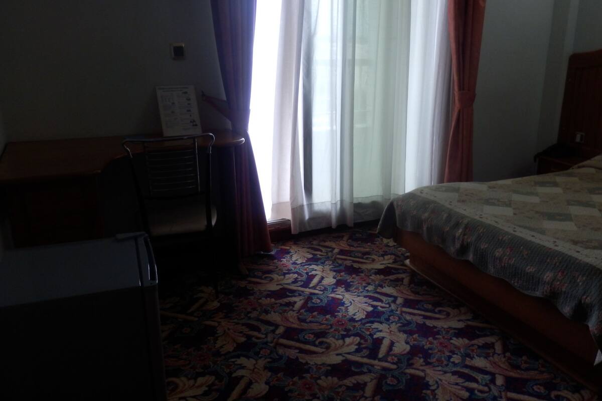 A hotel room with a bed, a desk, and a window with curtains.