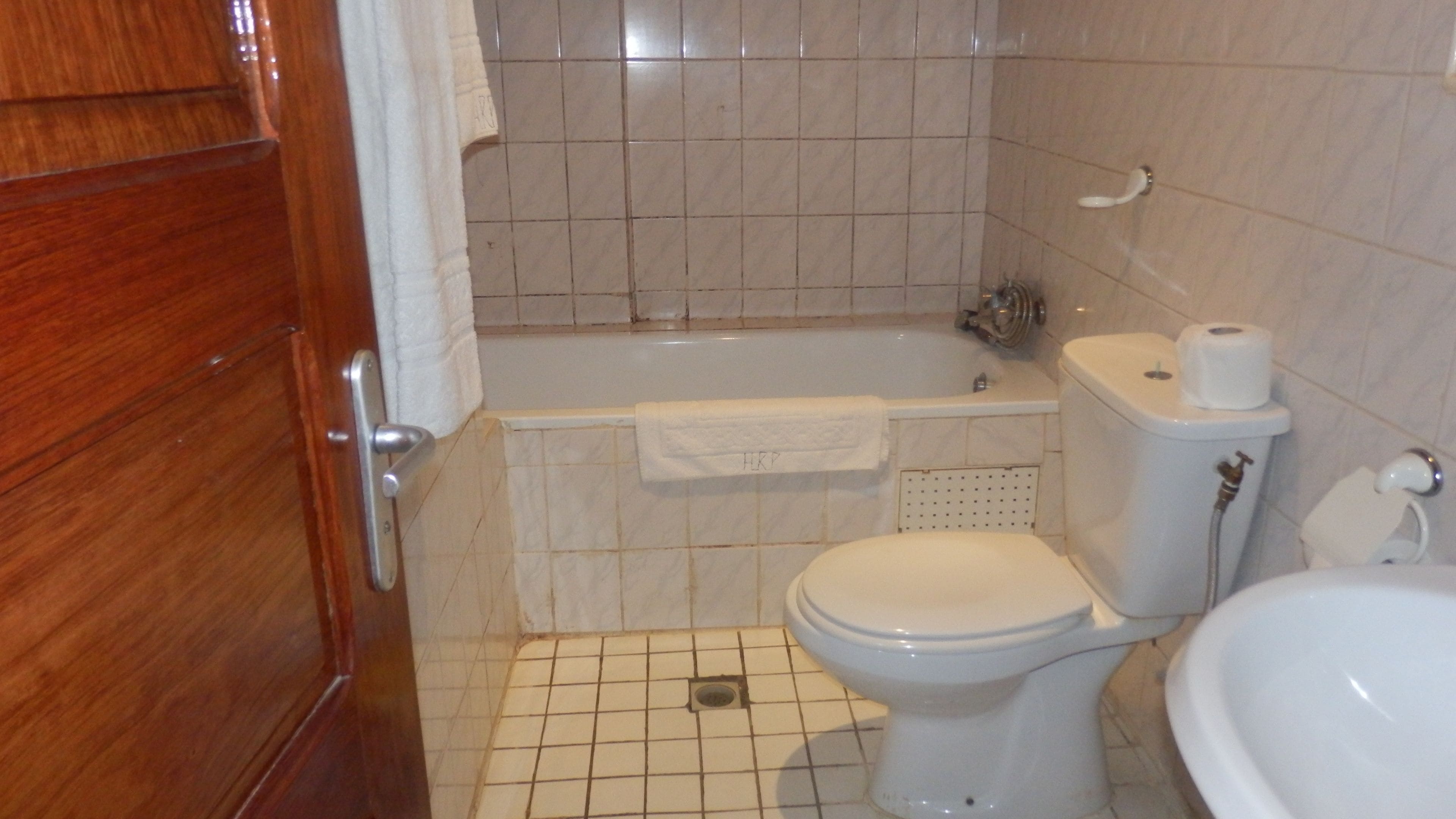 Un baño con puerta de madera, inodoro blanco, bañera y lavamanos.