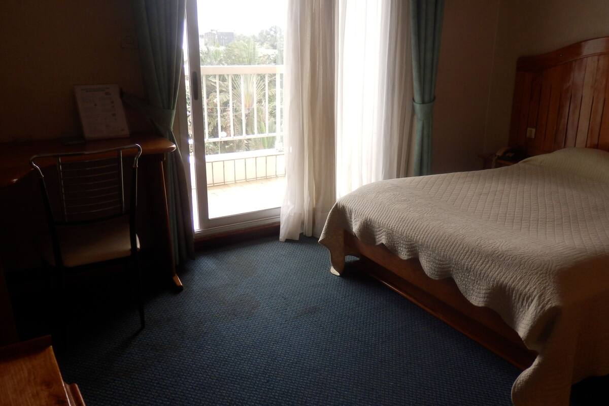 A hotel room with a bed, a desk, and a window with curtains.