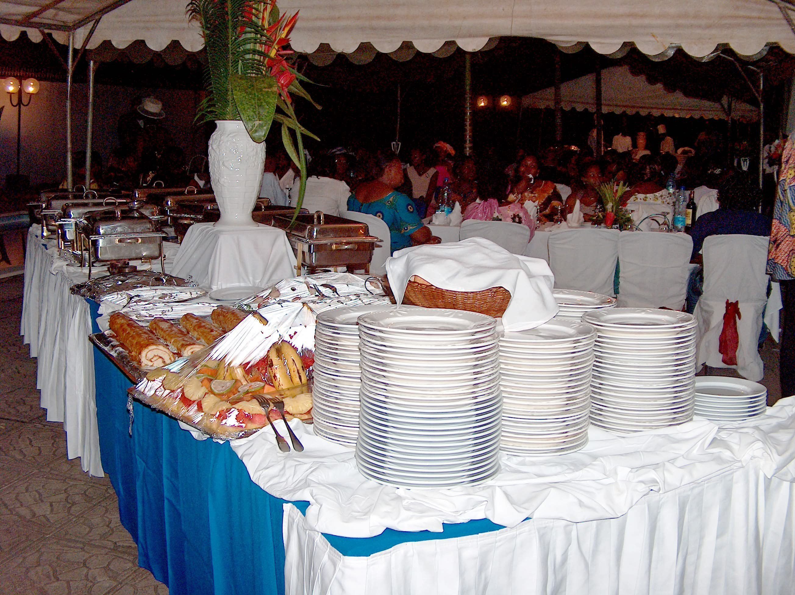 A buffet setup with various food items and stacked plates, under a tent.