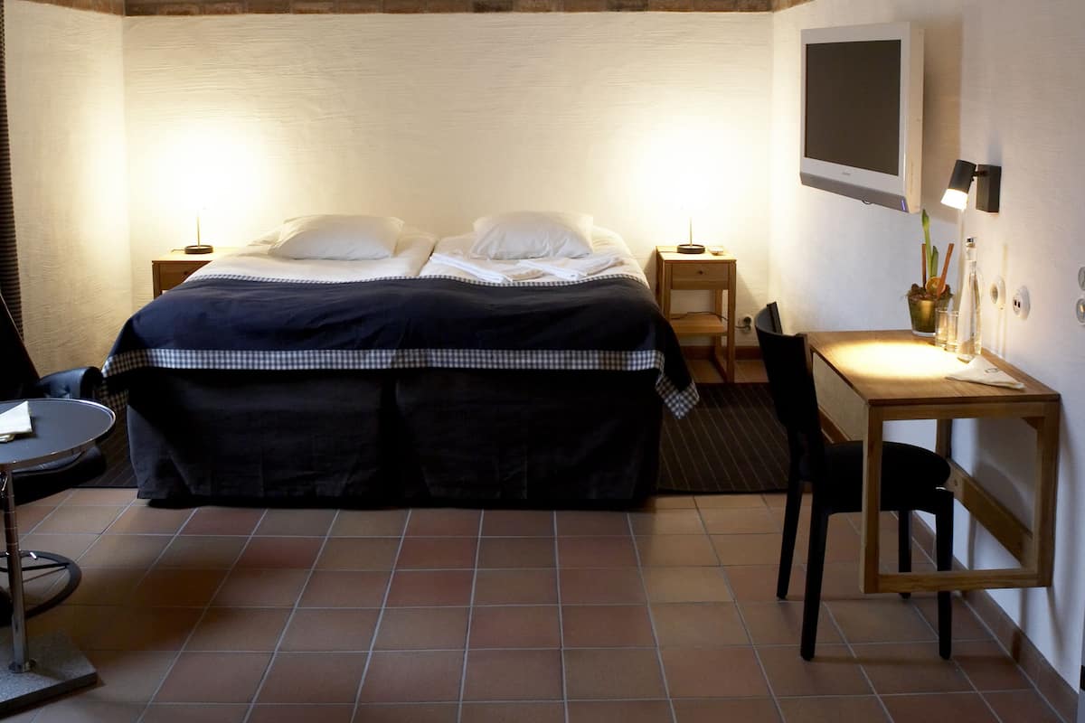 Una habitación de hotel con cama, escritorio, silla, televisor y lámpara.