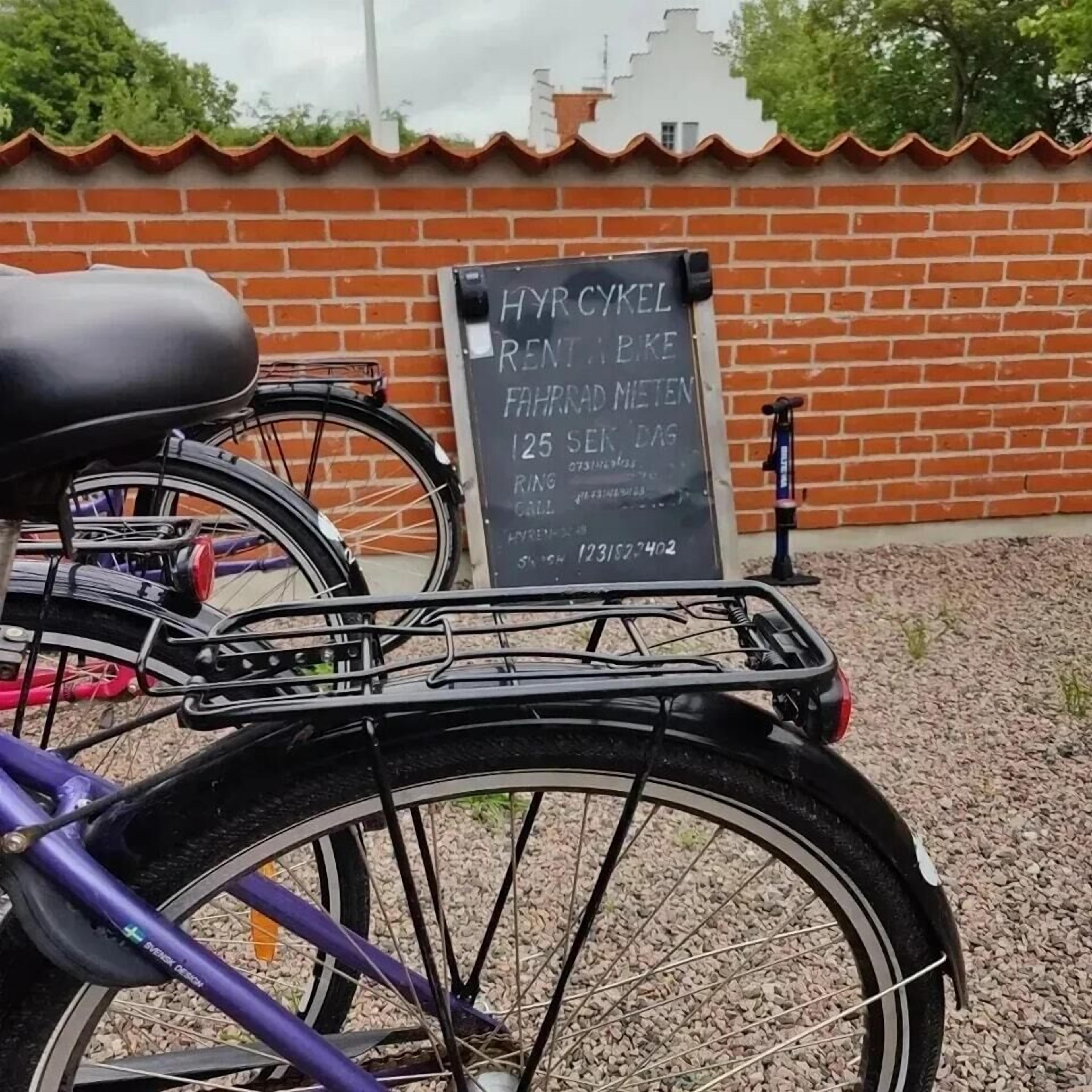A bicycle parked in front of a brick wall with a signboard displaying rental information.