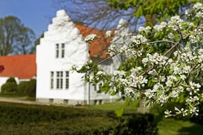 A white building with a red roof, surrounded by greenery and a clear sky.
