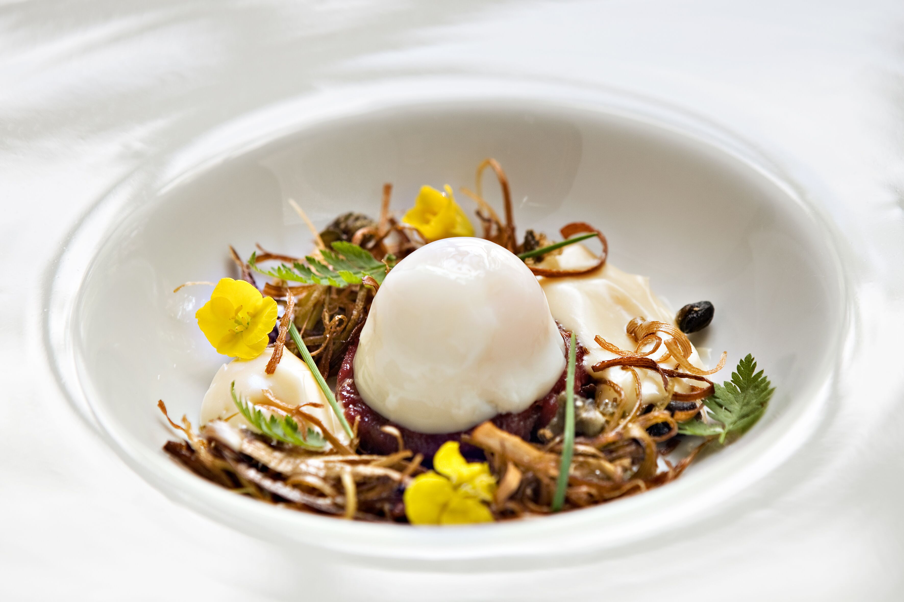 Eine weiße Schüssel mit pochiertem Ei, Grünzeug und essbaren Blüten.