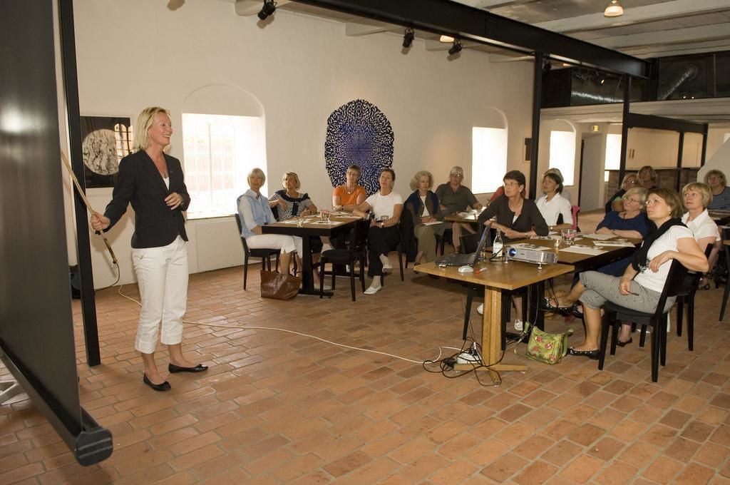 A conference room with a modern design, featuring a large abstract art piece on the wall, a brick floor, and a group of people seated at tables.