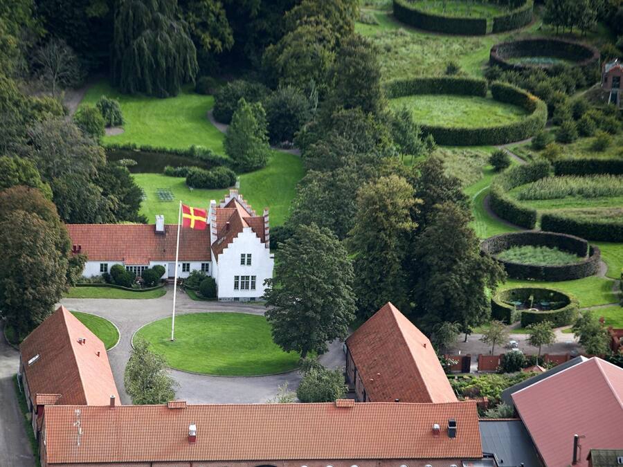 An aerial view of a property with a large white building featuring a red-tiled roof, surrounded by well-maintained gardens and hedgerows.