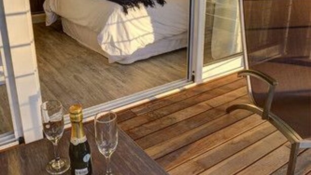 A bedroom with a bed, a bedside table with a bottle and glasses, and a chair. - 2122 Hotel Art Design (Punta del Este)