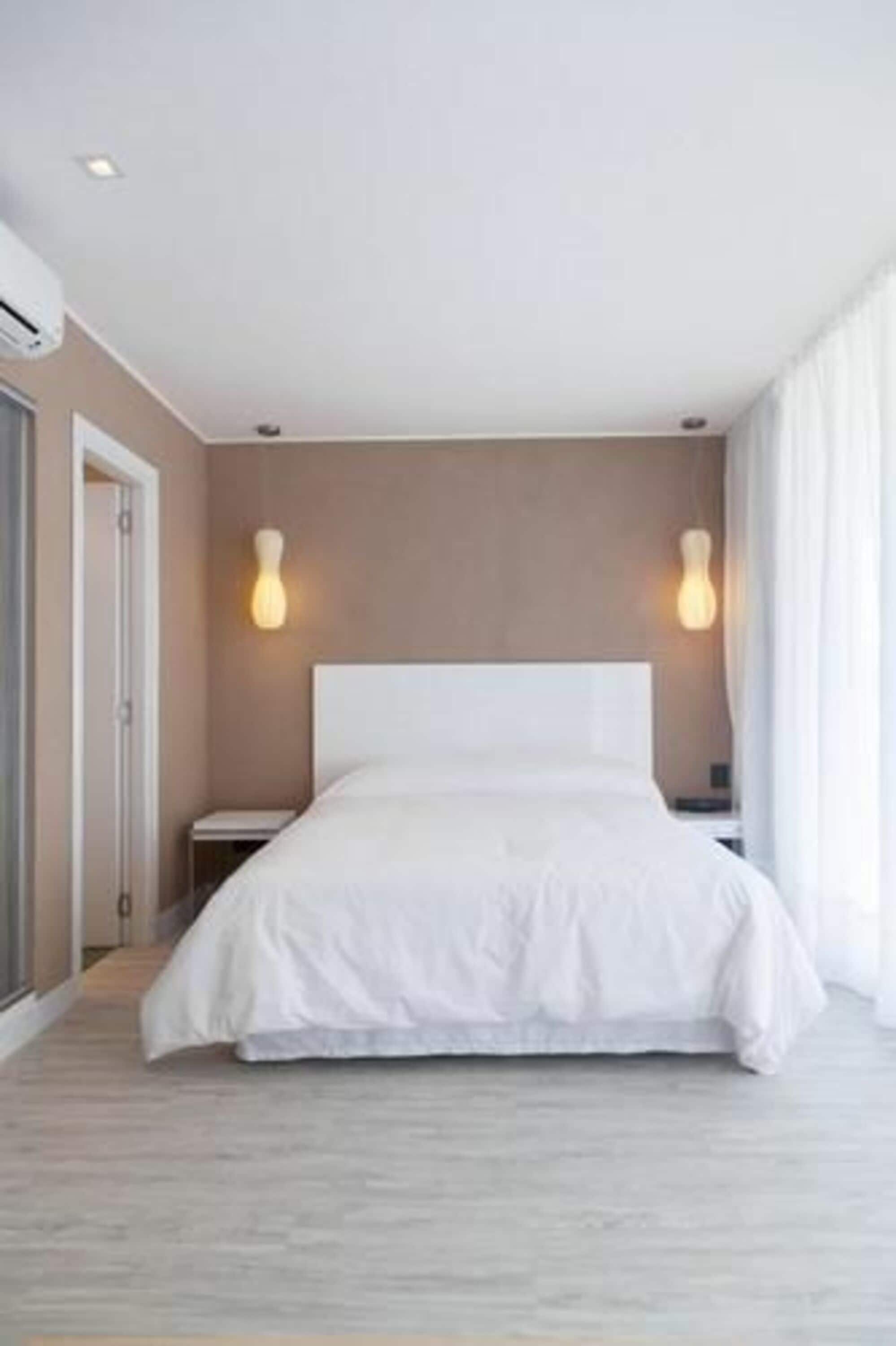 Una habitación de hotel moderna con una cama grande, dos mesitas de noche y una lámpara fijada a la pared.
