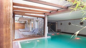 An indoor swimming pool with a wooden deck and lounge chairs, surrounded by stone walls and a tiled ceiling. - 2122 Hotel Art Design (Punta del Este)