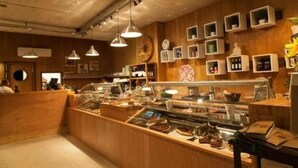 A bakery with a wooden interior, display cases with baked goods, and hanging pendant lights. - 2122 Hotel Art Design (Punta del Este)