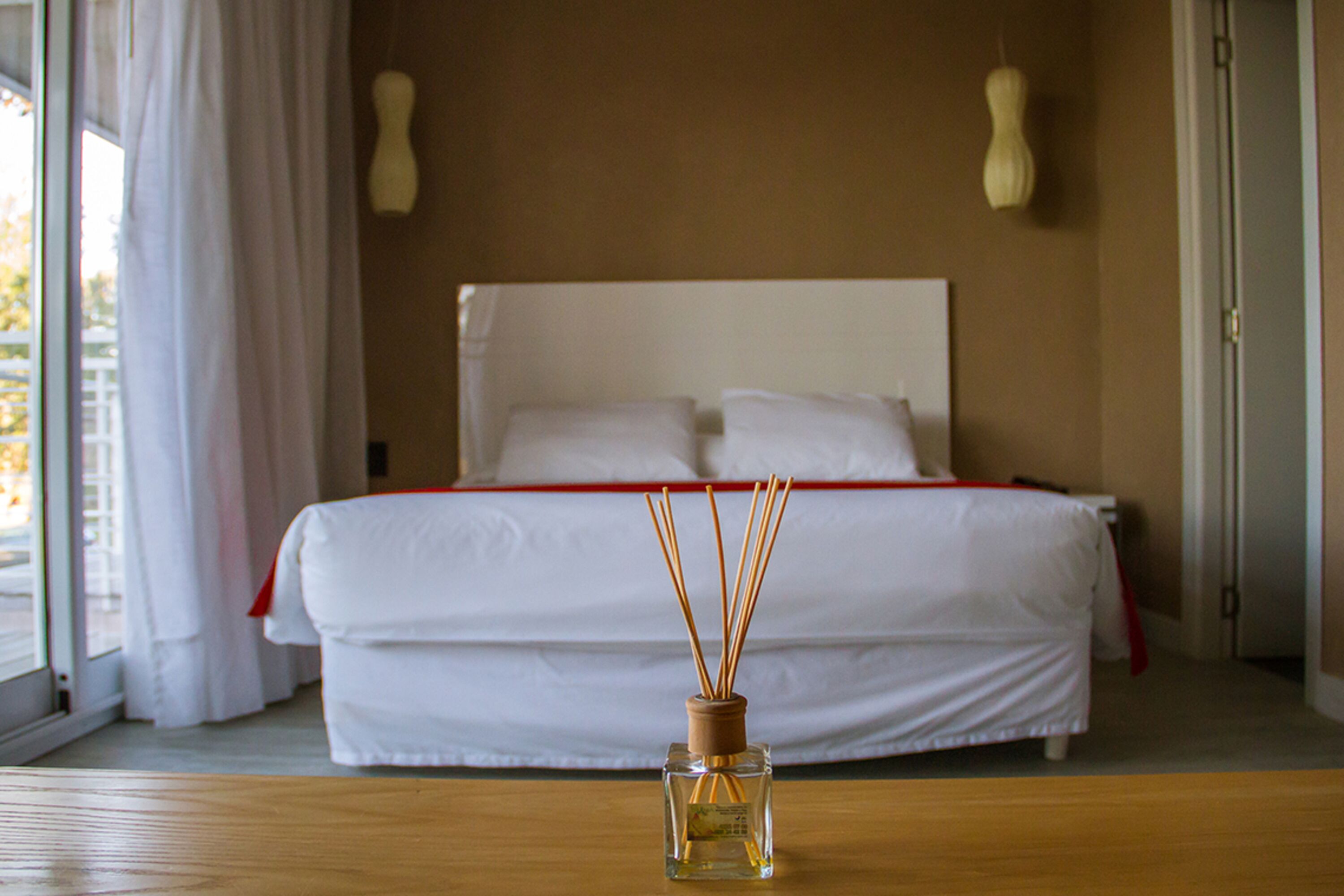 A hotel room with a bed, a wooden table, and a bottle of reed diffuser in the foreground.