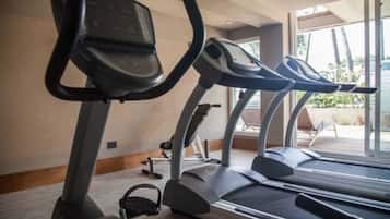 A row of treadmills in a well-lit room with large windows, a wooden floor, and a view of the outdoors.