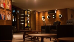 A modern lounge area with round tables and comfortable seating, a bookshelf, and decorative wall lighting. - 2122 Hotel Art Design (Punta del Este)