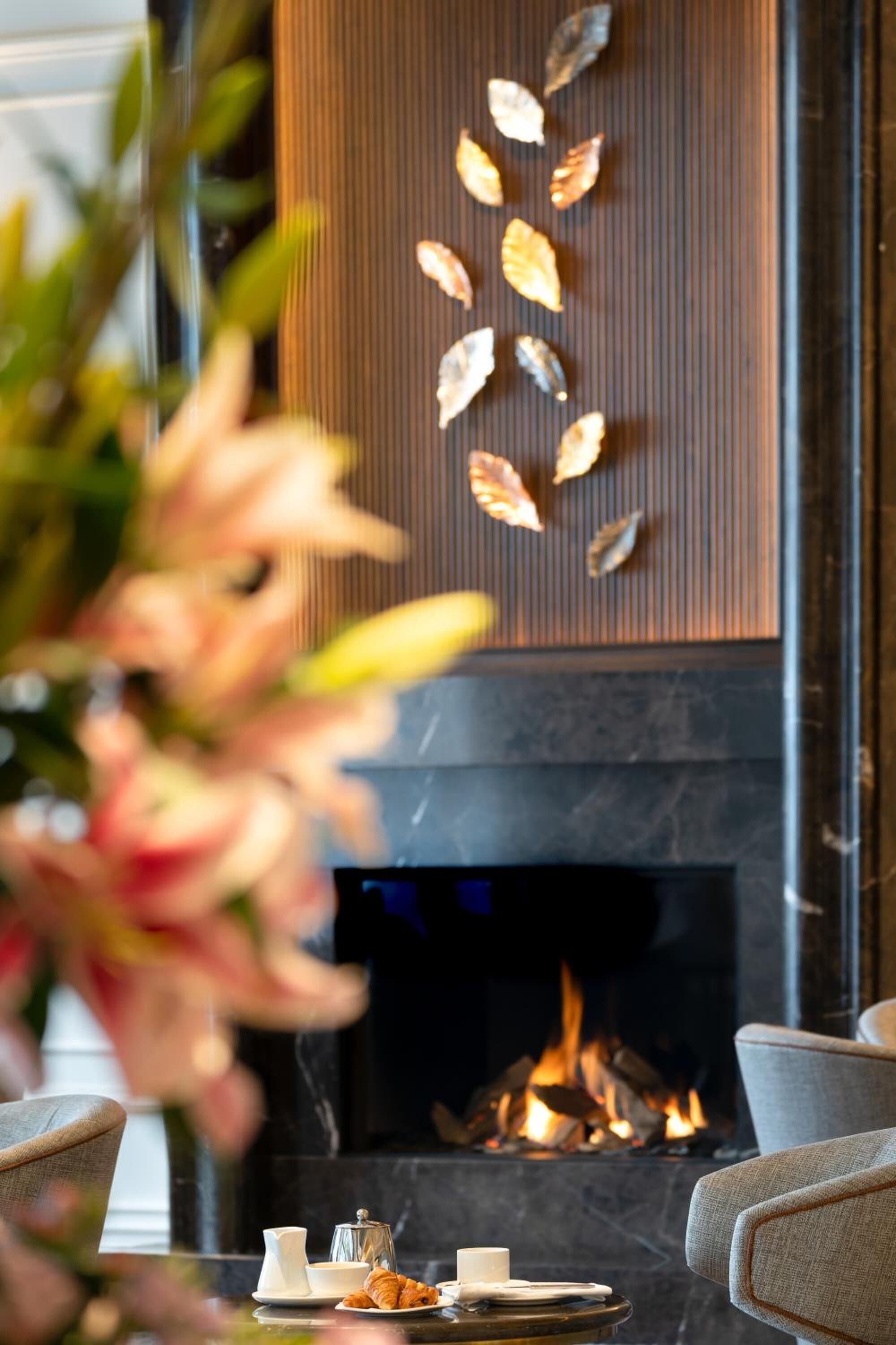 A cozy room with a fireplace, a table with a croissant, and a vase of flowers.