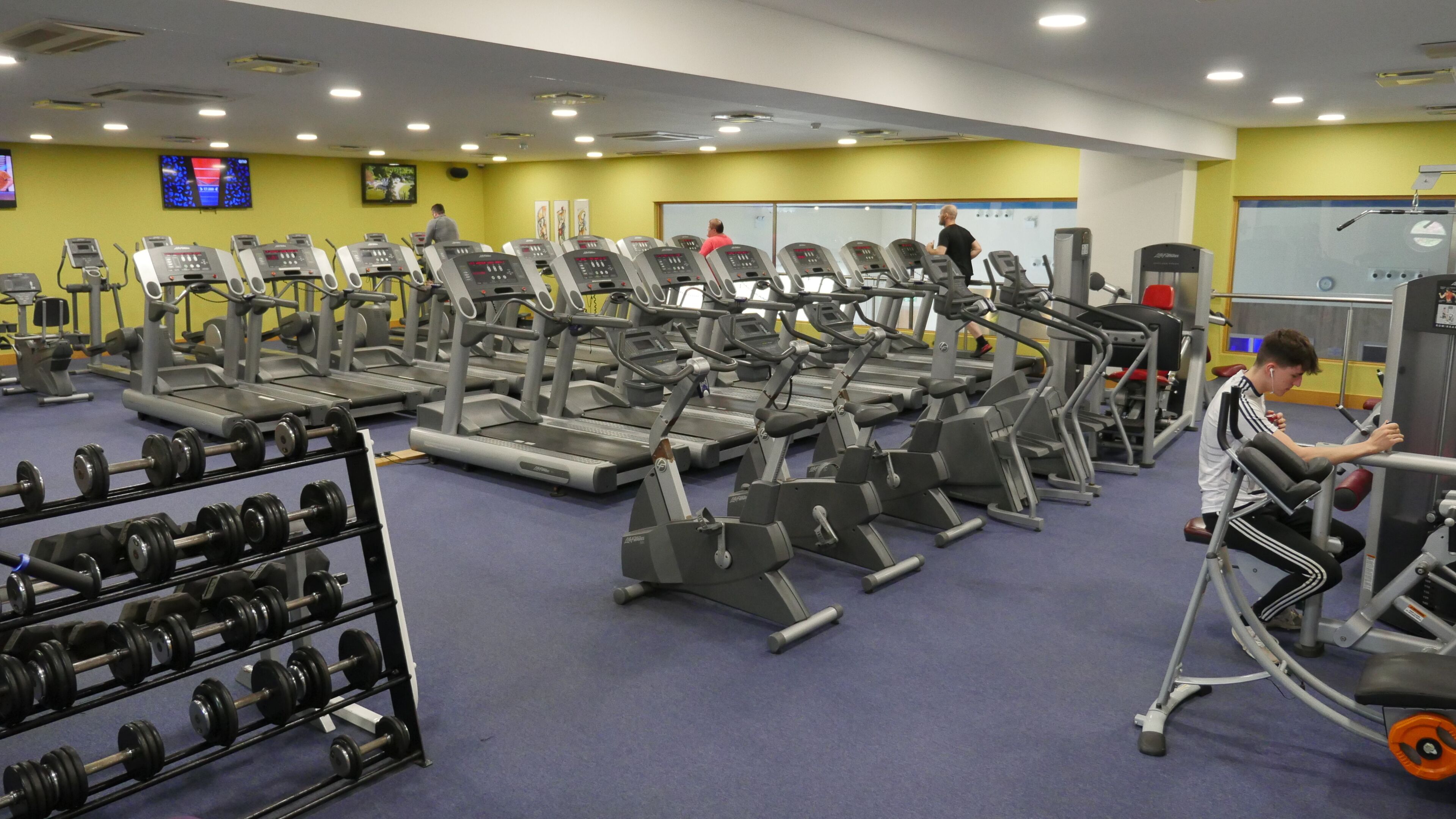 Ein Fitnessstudio mit Laufbändern, Krafttrainingsgeräten und Kurzhanteln.