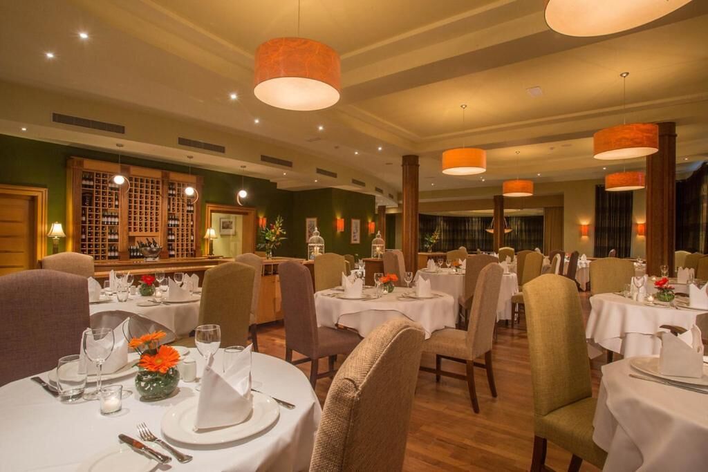 Un restaurante con mesas redondas dispuestas para comer, con manteles blancos y cubertería ordenada.
