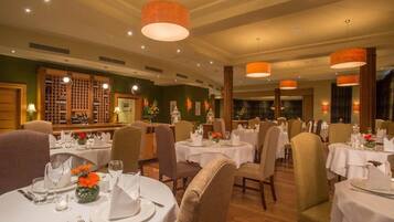 Un restaurante con mesas redondas dispuestas para comer, con manteles blancos y cubertería ordenada.