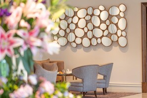 A modern interior with a wall-mounted mirror art piece, a seating area with a table, and a floral arrangement. - Mullingar Park Hotel (Mullingar)