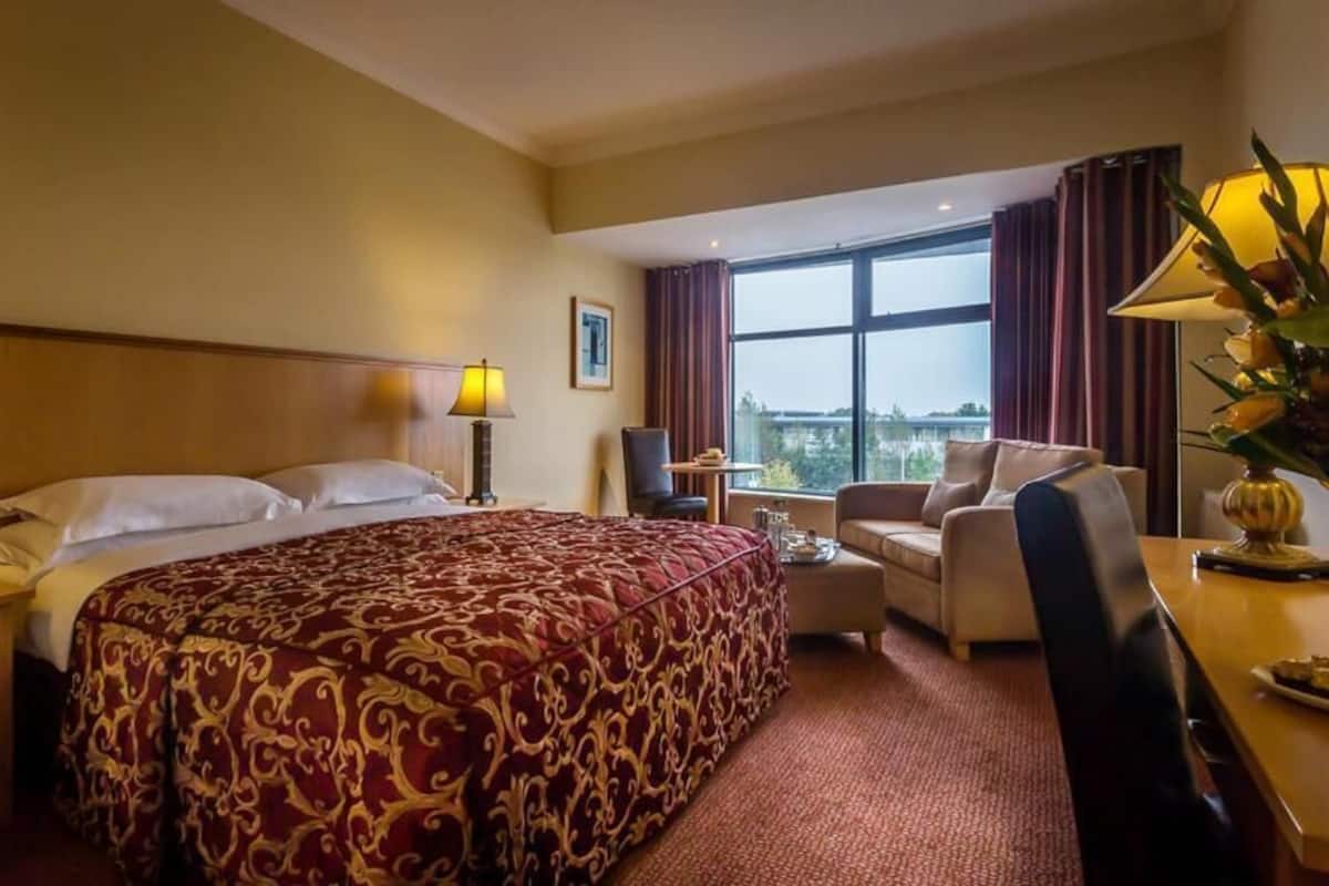 Habitación de hotel con una cama grande, un escritorio, una silla y vistas al exterior.