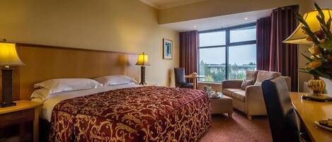 A hotel room with a large bed, a desk, a chair, and a view of the outdoors.