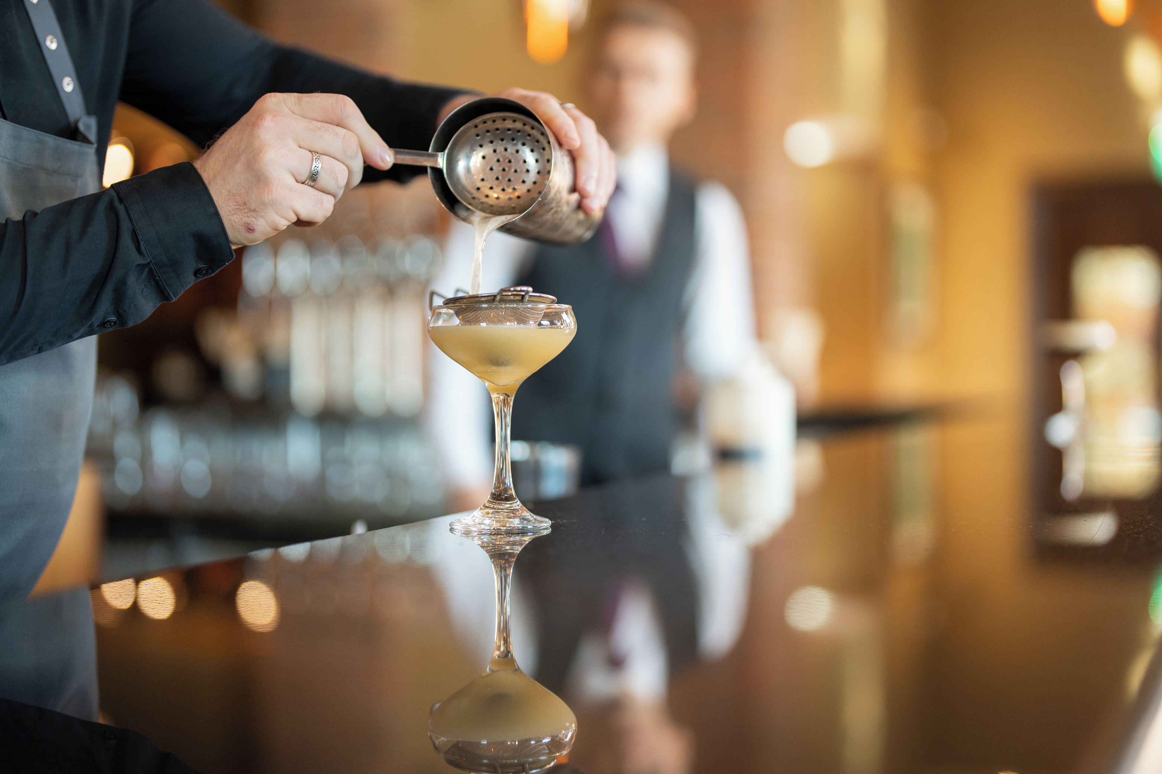 A bartender pouring a drink into a martini glass.