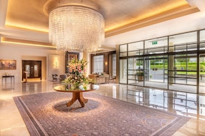 A lobby with a large chandelier, a round table with flowers, and a view of the outside through large windows. - Mullingar Park Hotel (Mullingar)